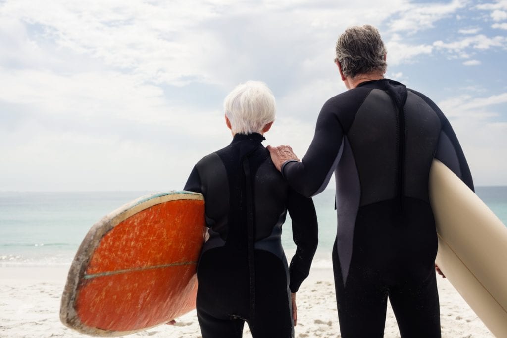 Senior couple in wetsuit holding surfboard on beach