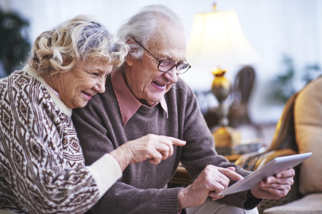 Elderly husband and wife with touchpad networking at leisure