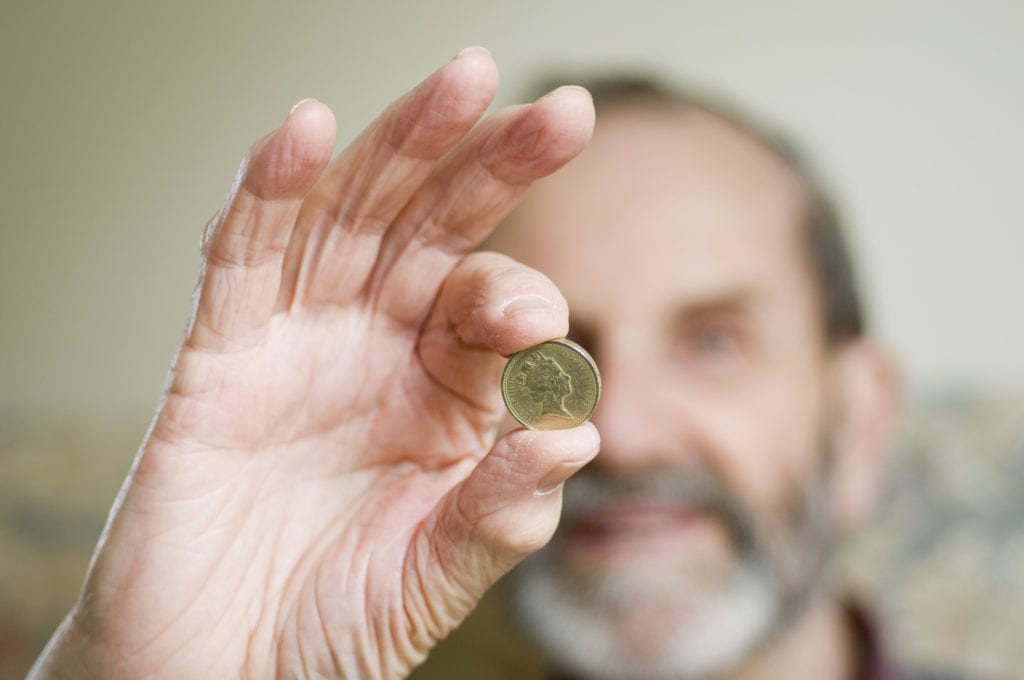 Senior man holding up a British one pound coin.